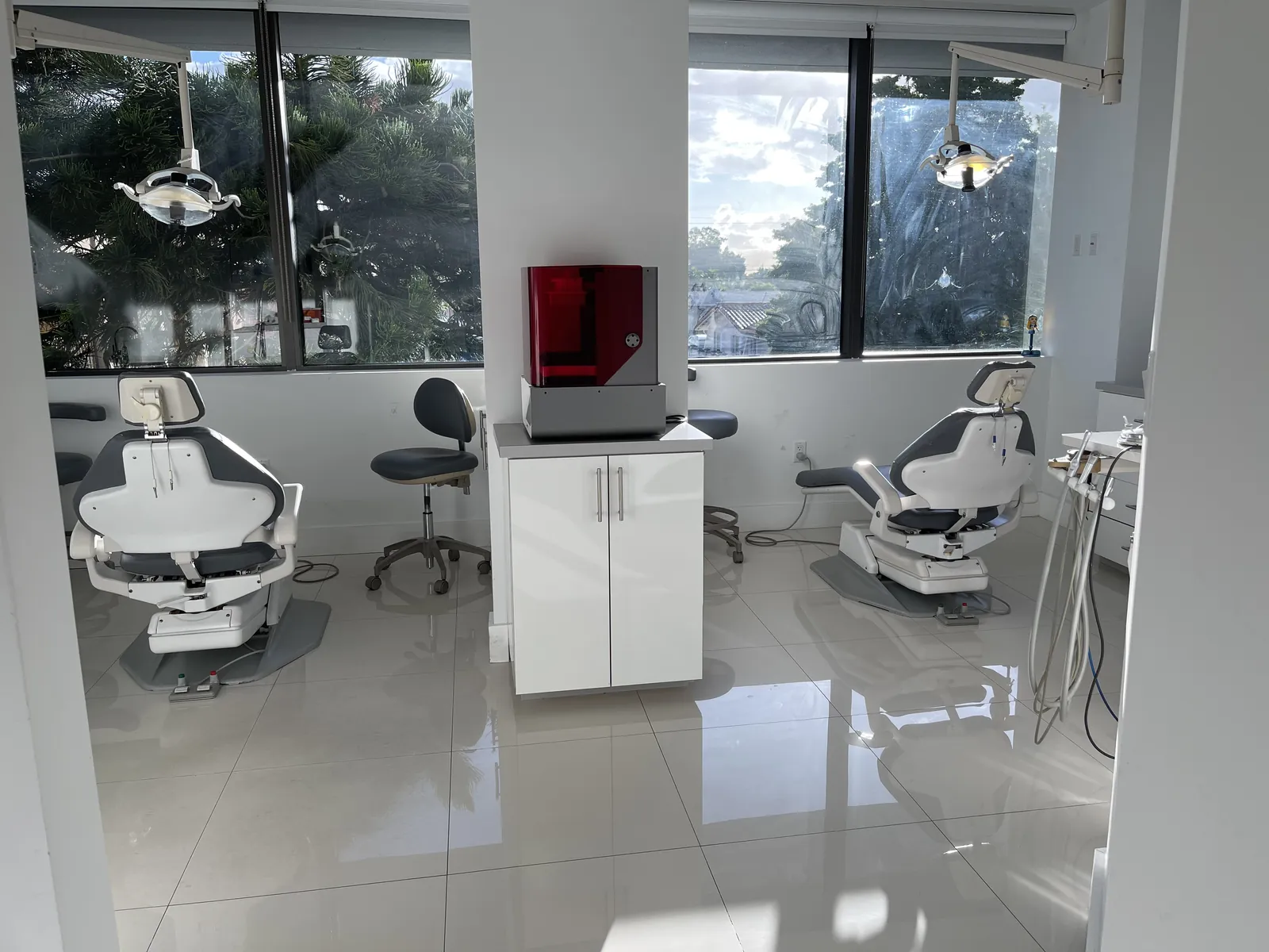 Bright operatory with two dental chairs and the in-house 3D printer under a translucent red cover