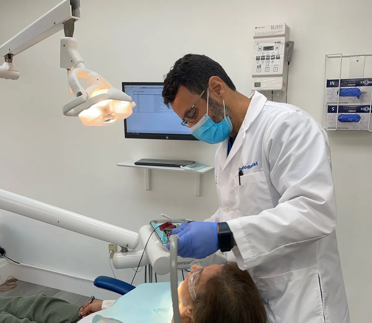 Dr. Roy Rosado, whose coat reads Prosthodontist, treating a patient in a bright operatory